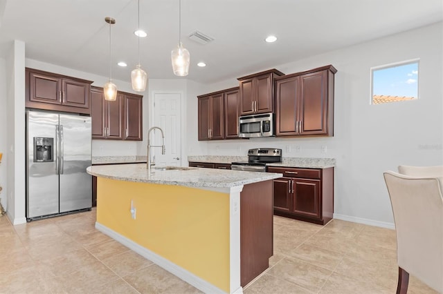 kitchen with light stone counters, stainless steel appliances, sink, decorative light fixtures, and a center island with sink