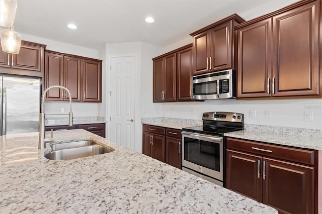 kitchen with light stone counters, sink, hanging light fixtures, and appliances with stainless steel finishes