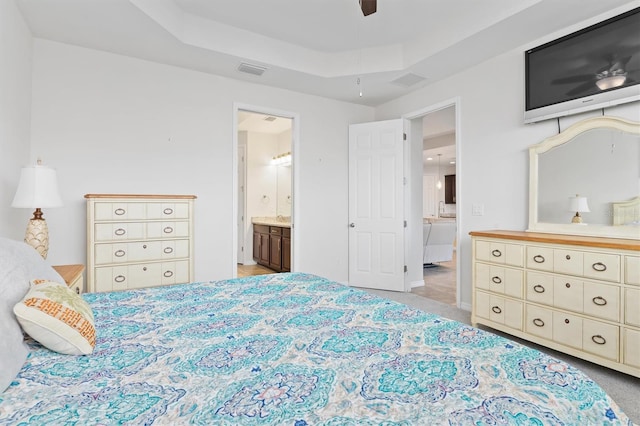 bedroom featuring a raised ceiling, ensuite bath, ceiling fan, and light colored carpet