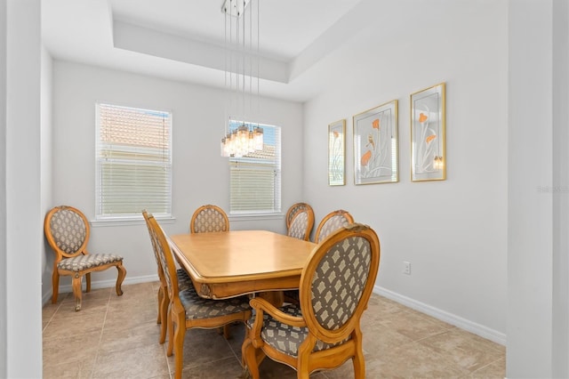 dining room with light tile patterned floors, a raised ceiling, and baseboards