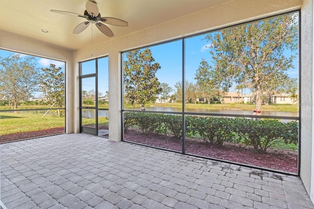 unfurnished sunroom featuring ceiling fan and a water view