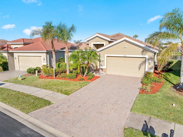 mediterranean / spanish home with stucco siding, decorative driveway, a front yard, an attached garage, and a tiled roof