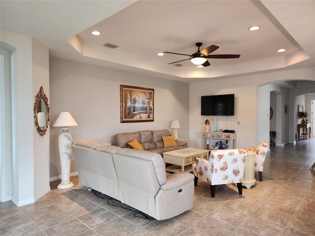 living room featuring visible vents, a ceiling fan, baseboards, arched walkways, and a raised ceiling