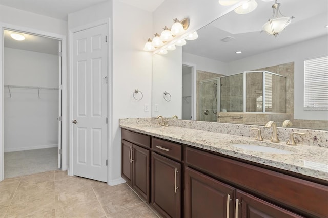 bathroom featuring double vanity, a stall shower, a spacious closet, and a sink