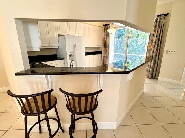 kitchen with a kitchen breakfast bar, white fridge with ice dispenser, kitchen peninsula, and white cabinetry