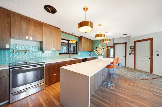 kitchen with a kitchen breakfast bar, light hardwood / wood-style flooring, stainless steel stove, a kitchen island, and hanging light fixtures