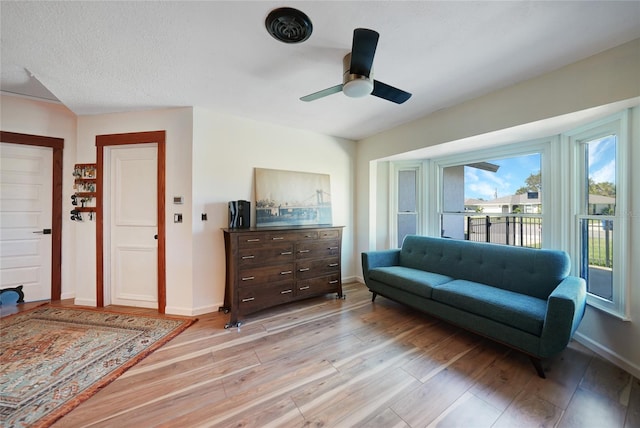 living room with ceiling fan, light hardwood / wood-style flooring, and a textured ceiling