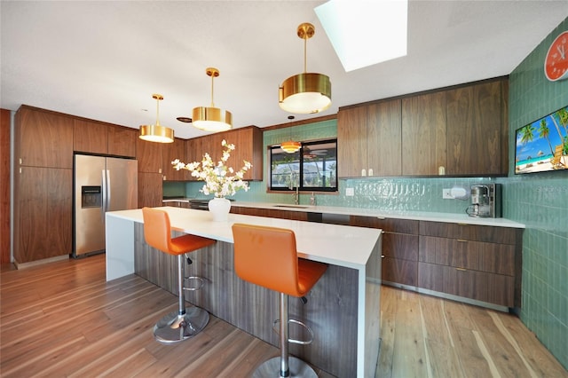 kitchen with a breakfast bar area, light hardwood / wood-style flooring, pendant lighting, and stainless steel refrigerator with ice dispenser