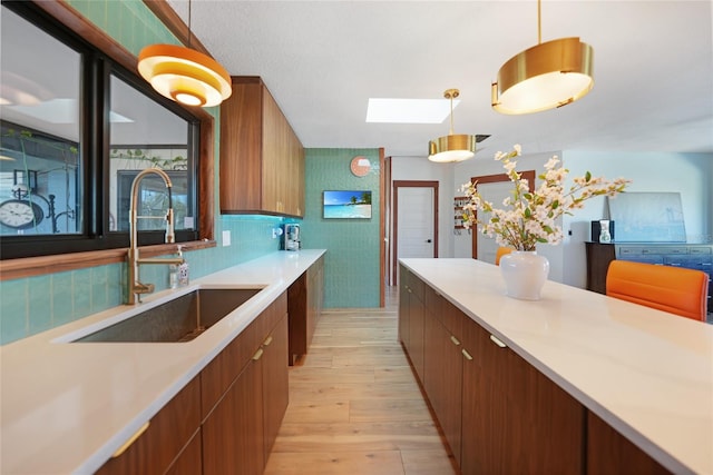 kitchen featuring backsplash, a skylight, sink, decorative light fixtures, and light hardwood / wood-style flooring