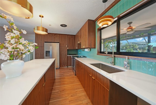 kitchen with a textured ceiling, sink, stainless steel appliances, and decorative light fixtures