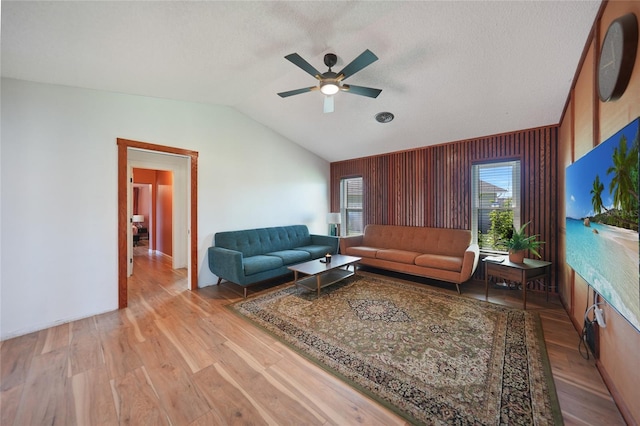 living room with a textured ceiling, vaulted ceiling, ceiling fan, light hardwood / wood-style floors, and wood walls