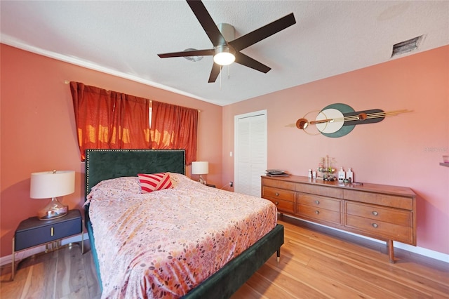 bedroom featuring a textured ceiling, a closet, light hardwood / wood-style floors, and ceiling fan