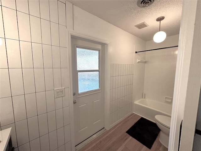 bathroom featuring bathtub / shower combination, hardwood / wood-style flooring, toilet, a textured ceiling, and tile walls