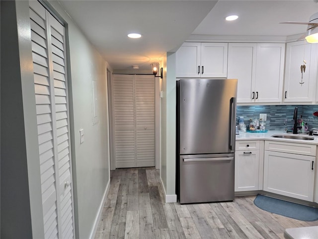 kitchen featuring backsplash, sink, light wood-type flooring, white cabinetry, and stainless steel refrigerator