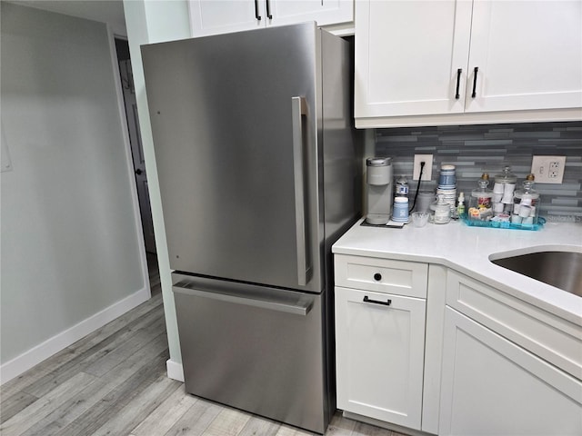 kitchen featuring white cabinets, light wood-type flooring, stainless steel refrigerator, and tasteful backsplash