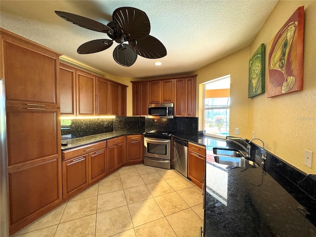 kitchen with decorative backsplash, stainless steel appliances, sink, dark stone countertops, and light tile patterned flooring