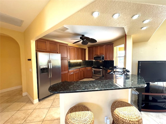 kitchen with backsplash, a breakfast bar area, a textured ceiling, kitchen peninsula, and stainless steel appliances