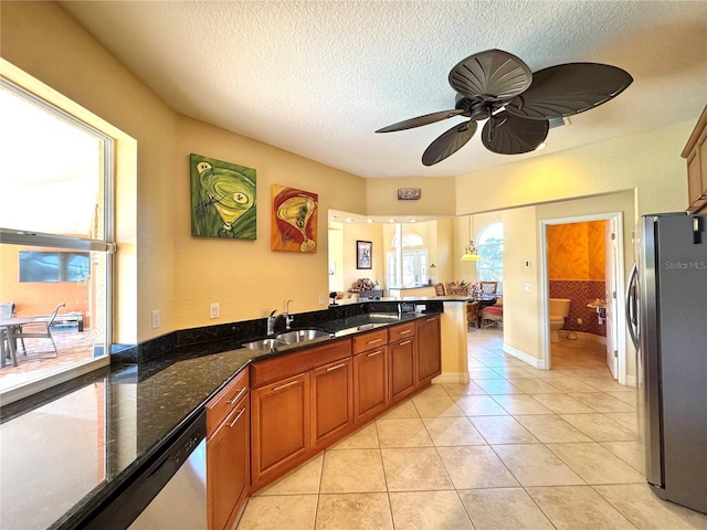 kitchen with ceiling fan, sink, stainless steel appliances, kitchen peninsula, and dark stone countertops