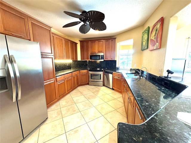 kitchen with decorative backsplash, appliances with stainless steel finishes, dark stone counters, ceiling fan, and sink