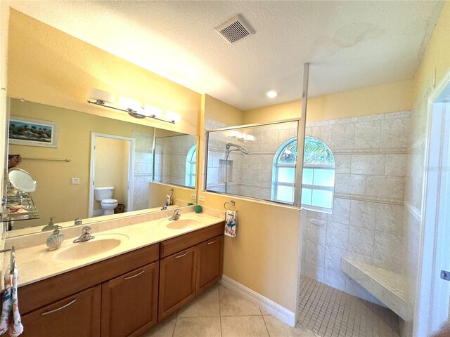 bathroom with tile patterned floors, a tile shower, vanity, a textured ceiling, and toilet