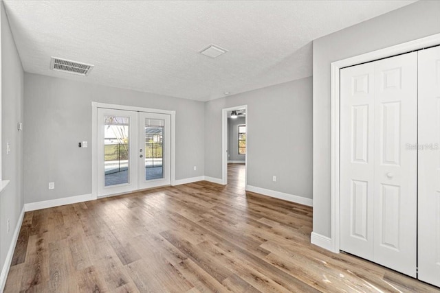 spare room with french doors, a textured ceiling, and light hardwood / wood-style floors