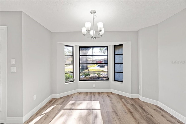 unfurnished dining area with a chandelier, a textured ceiling, and light hardwood / wood-style floors