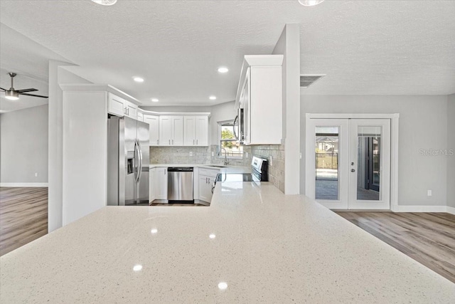 kitchen with light hardwood / wood-style floors, white cabinetry, a textured ceiling, and appliances with stainless steel finishes