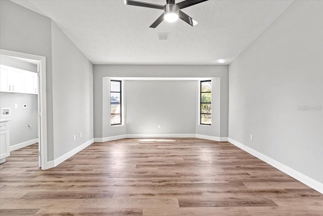 empty room with ceiling fan, light wood-type flooring, and a textured ceiling