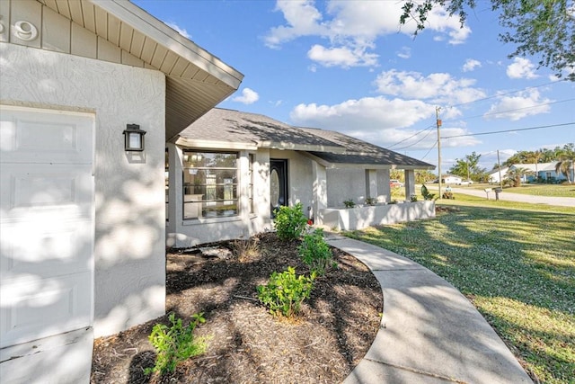 entrance to property featuring stucco siding, a yard, roof with shingles, and a garage