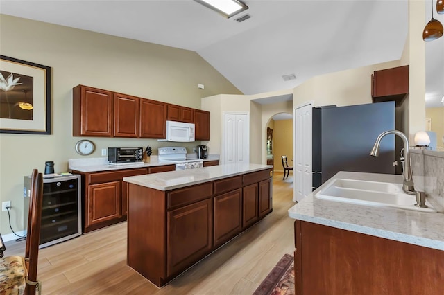 kitchen with lofted ceiling, white appliances, sink, light stone countertops, and beverage cooler