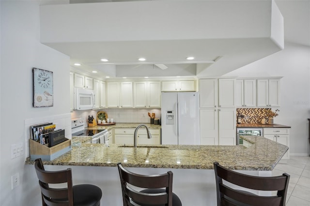 kitchen with white cabinetry, sink, stone counters, kitchen peninsula, and white appliances