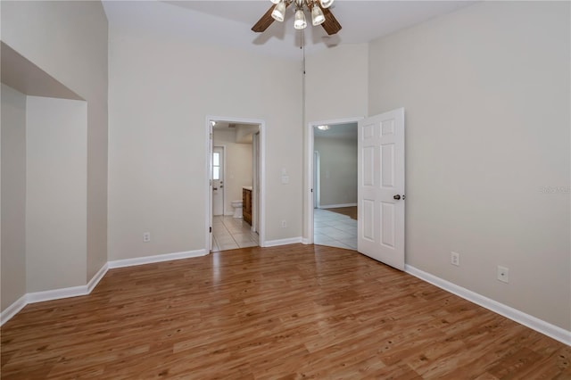 unfurnished bedroom with ceiling fan, light hardwood / wood-style floors, a high ceiling, and ensuite bath