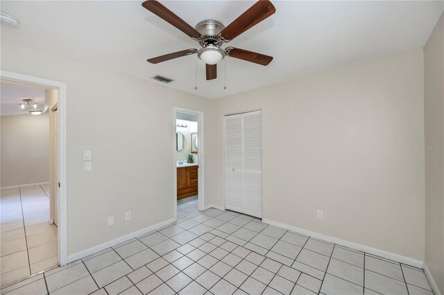 unfurnished bedroom with ensuite bathroom, ceiling fan, light tile patterned flooring, and a closet