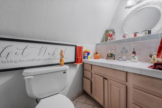 bathroom with vanity, lofted ceiling, tile patterned floors, toilet, and tasteful backsplash