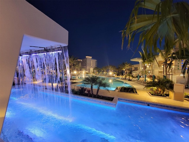 pool at night featuring pool water feature