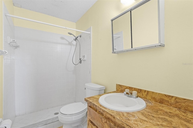 bathroom featuring vanity, toilet, a textured ceiling, and a tile shower