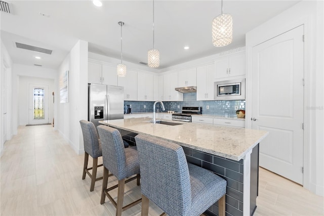 kitchen featuring white cabinets, appliances with stainless steel finishes, decorative light fixtures, and an island with sink