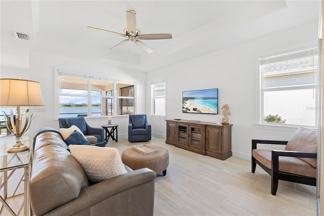 living room with a raised ceiling, ceiling fan, and a healthy amount of sunlight