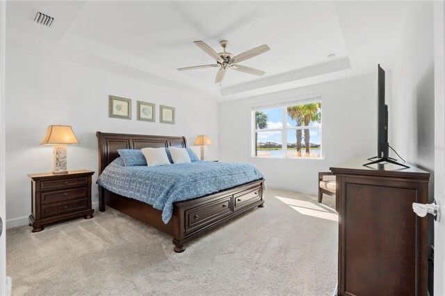 carpeted bedroom with ceiling fan and a tray ceiling