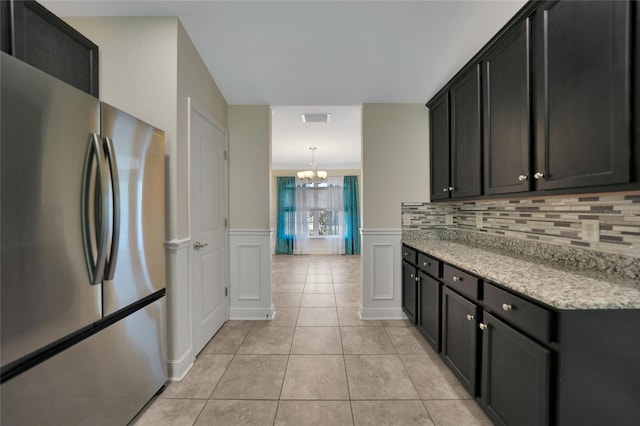 kitchen with an inviting chandelier, hanging light fixtures, decorative backsplash, light tile patterned flooring, and stainless steel refrigerator