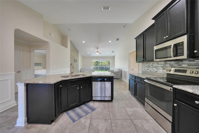 kitchen featuring light stone countertops, appliances with stainless steel finishes, a kitchen island with sink, and sink