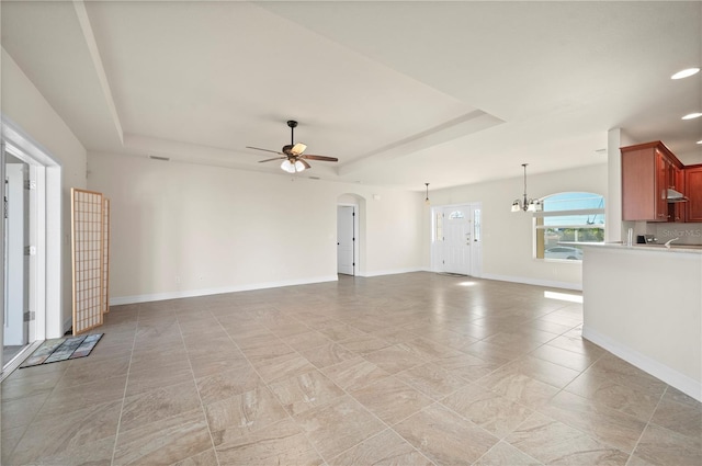 unfurnished living room with ceiling fan with notable chandelier and a tray ceiling