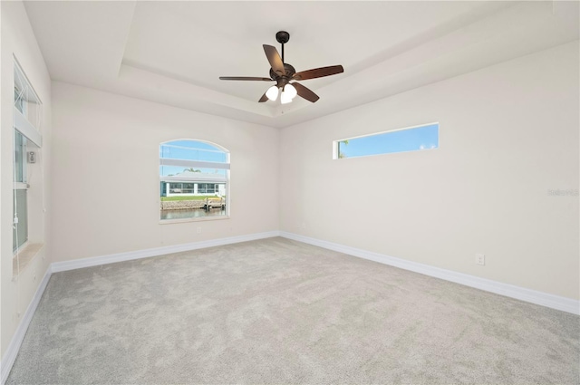 unfurnished room featuring ceiling fan, light carpet, and a tray ceiling