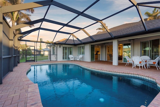 pool at dusk featuring a lanai, a patio area, and ceiling fan