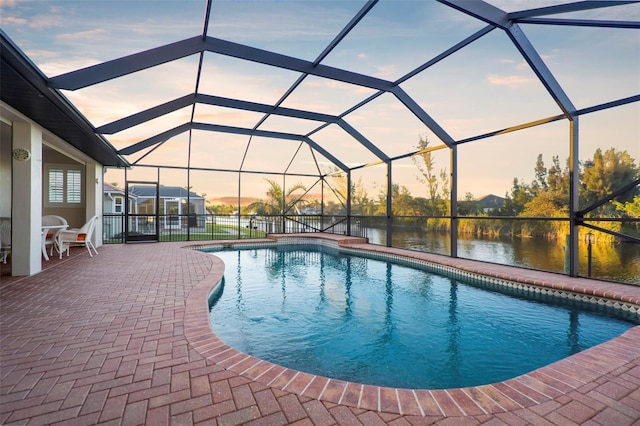 pool at dusk with a lanai, a patio area, and a water view