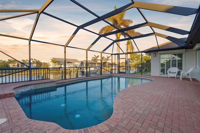 pool at dusk featuring a lanai, a water view, and a patio