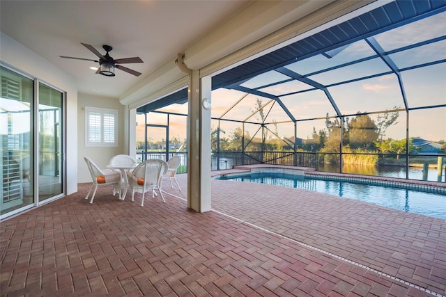 pool at dusk with glass enclosure, ceiling fan, and a patio area