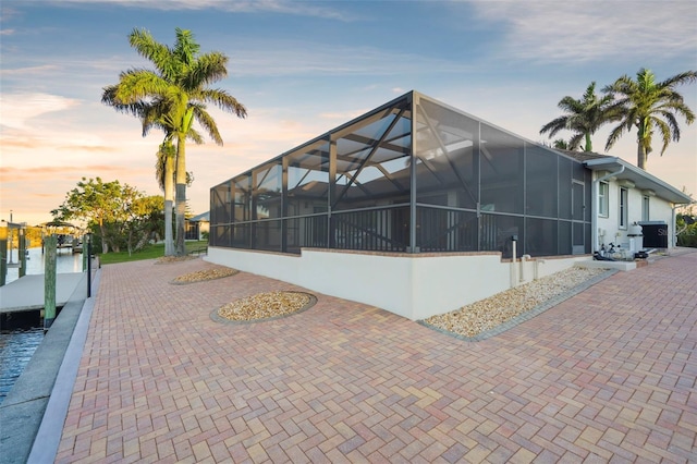 exterior space featuring a boat dock, a water view, a patio, and glass enclosure