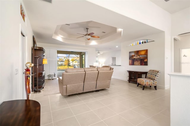 tiled living room with ceiling fan and a tray ceiling