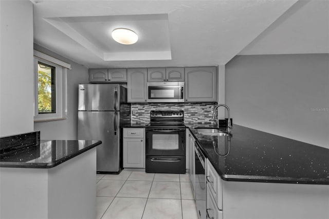 kitchen with dark stone counters, sink, gray cabinets, kitchen peninsula, and stainless steel appliances